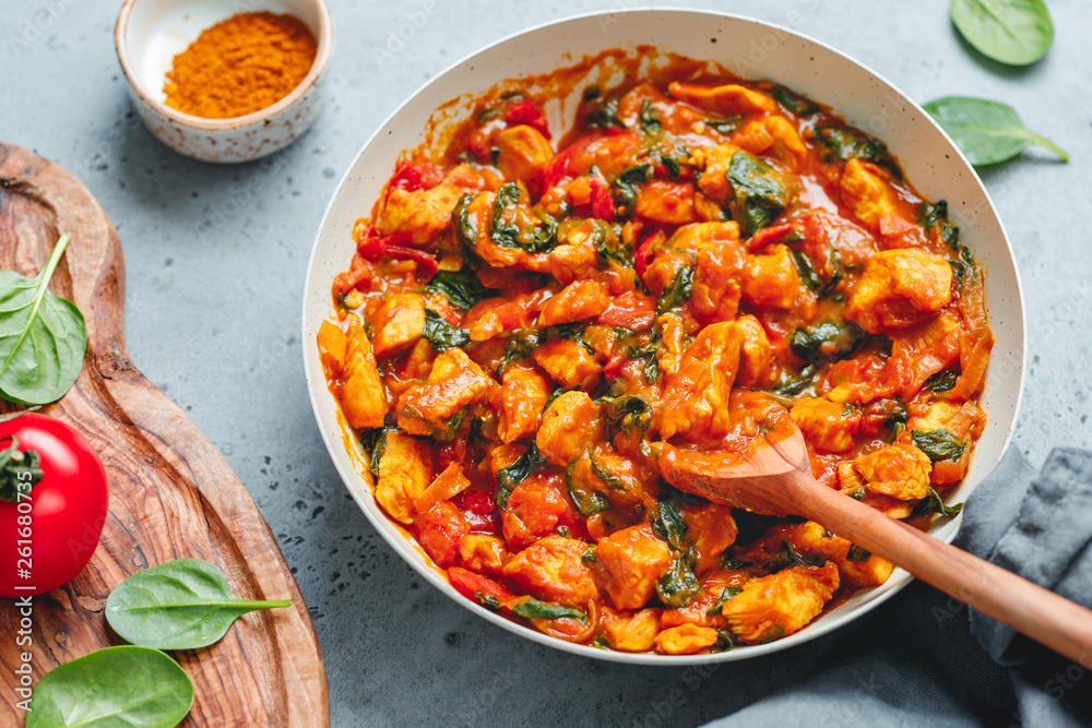 Bombay chicken curry with spinach, tomato and onion in a white frying pan on a kitchen table. Indian traditional cuisine. Bombay chicken curry with spinach, tomato and onion in a white frying pan on a kitchen table. Indian traditional cuisine.