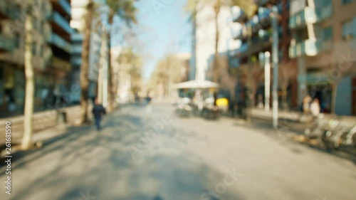 First-person POV handheld shot, slow motion: walking on a public street at day, everything is blurry and defocused.