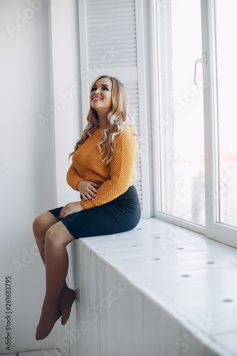 Elegant woman in a yellow sweater. Pregnant woman sitting near window