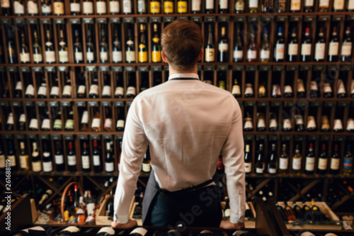 Fotografía Rack with wine bottles and bartender or cavist man backside on foreground
