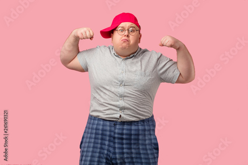 Comical home superhero with arrogant face wearing checkered huge shorts shows his muscles and competence isolated on pink background