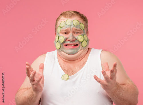 Desperate man gestures in puzzlement, being annoyed as has cucumber facial mask that irritates his skin. Mens Cosmetology, Mens grooming concept