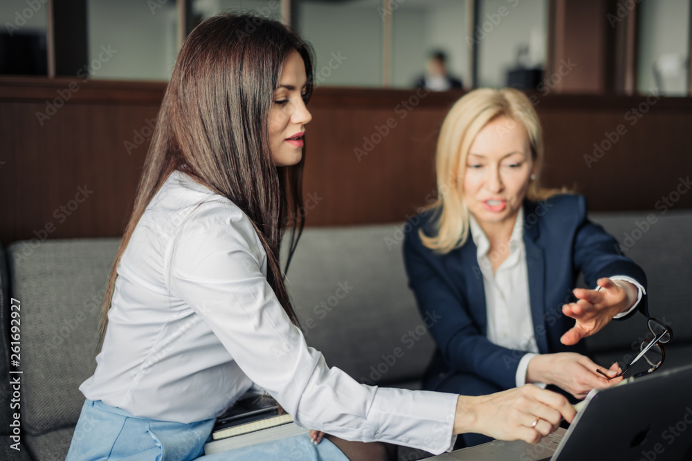 Two caucasian female coworkers working together on business project using laptop, female executive explaining new online idea to coworker at office Two caucasian female coworkers working together on business project using laptop, female executive explaining new online idea to coworker at office