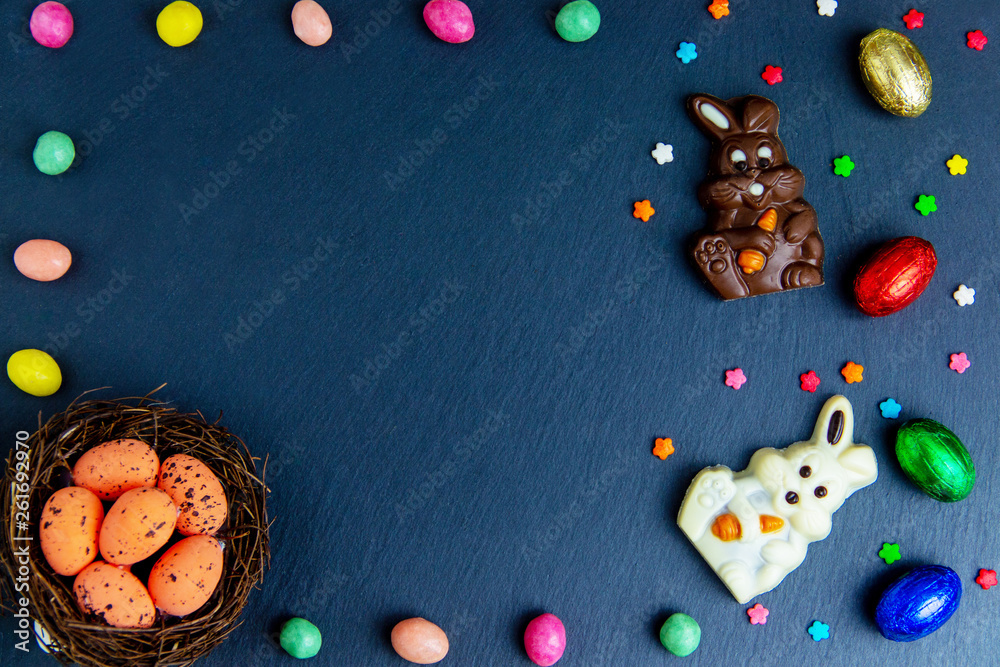 Fototapeta premium Easter eggs in the nest, chocolate eggs and candies. Top view on stone table with space for your greetings multicolor picture