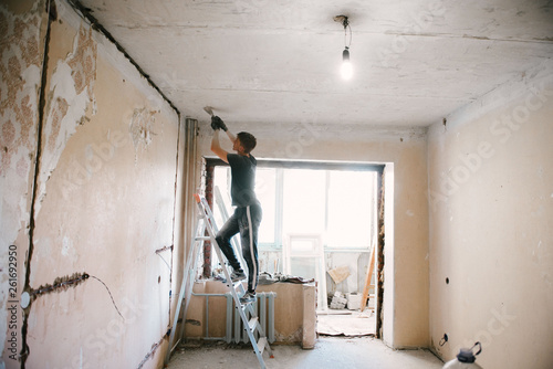 Принти на полотні A man removes old paint from the ceiling with a spatula
