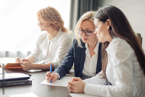 Three caucasian female students or interns in white shirts , intern using laptop, working on pc, studying in university, typing, browsing websites, apps, writing report, chatting in social network