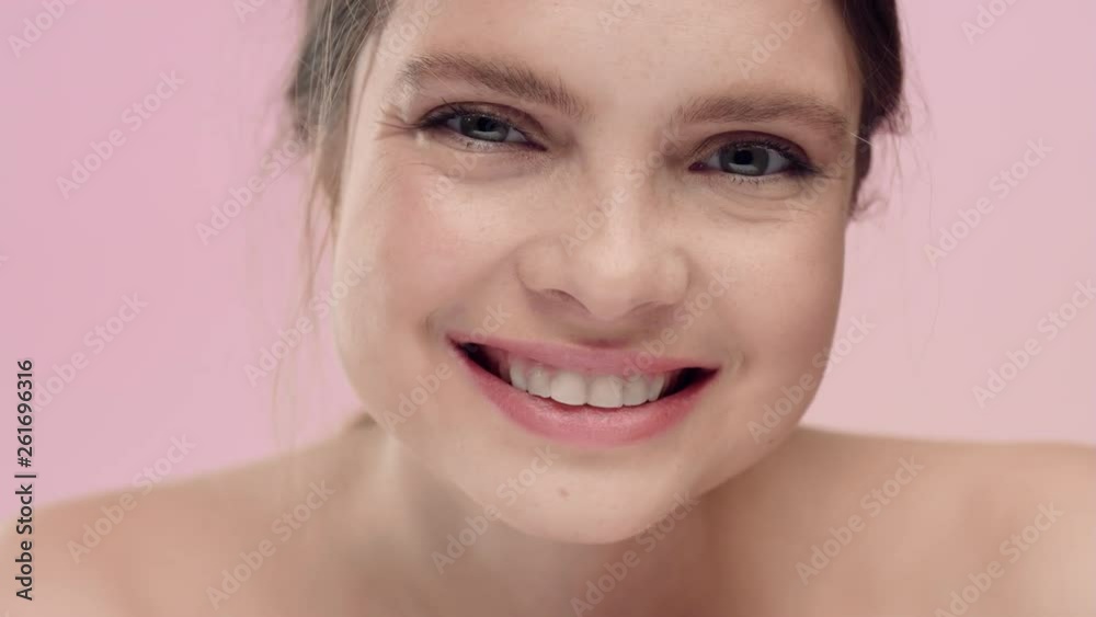 Young freckled woman looking at camera and smiling on pink bg