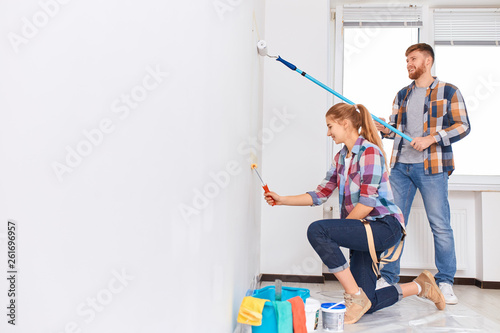 Couple in casual plaid shirts painting house wall together, side view. Painted walls today, despite the huge variety of finishing materials, are very popular.