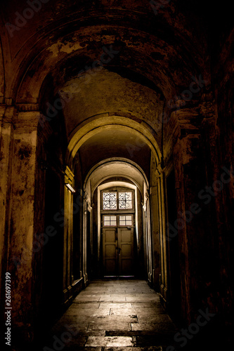 A gloomy corridor with a door at the end  from which comes the light