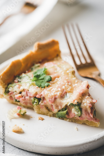 A piece of homemade cheese quiche or pie sprinkled with parsley on gray concrete background. Vintage toned. French cuisine