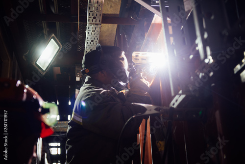 Worker in protective clothing and mask works with a welding machine.