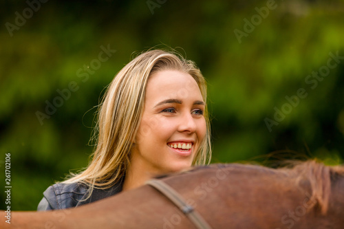 Close-up of smiling woman patting her arabian horse with grass in the field
