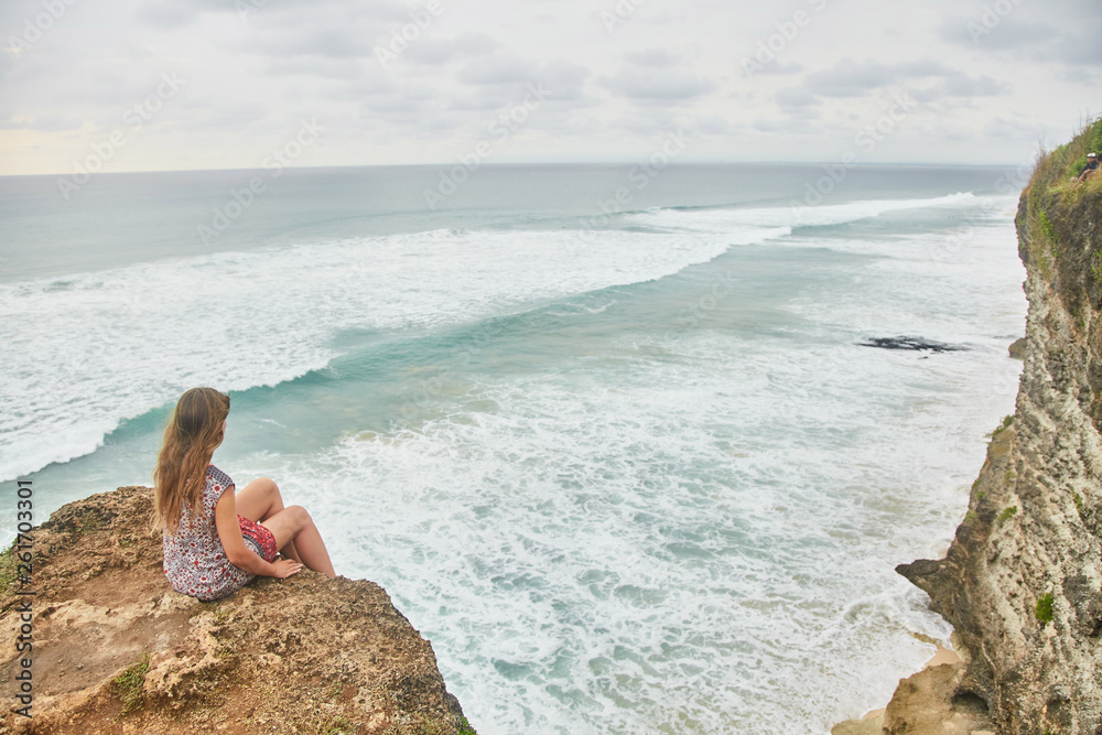 A young girl is sitting on a cliff. Bali, Uluwatu. 