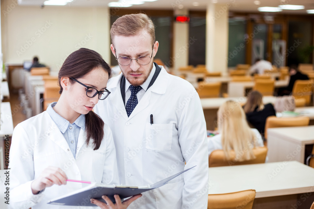 Joyful young general practitioner. Smiling professional doctor in white coat discussing diagnosis in library. Health concept Joyful young general practitioner. Smiling professional doctor in white coat discussing diagnosis in library. Health concept