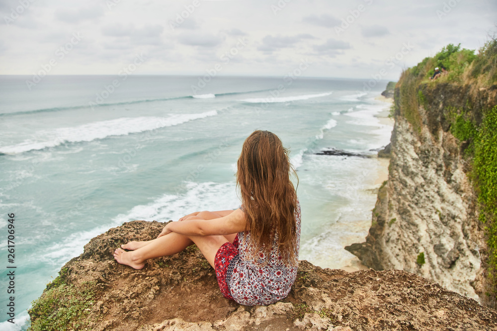 A young girl is sitting on a cliff. Bali, Uluwatu. 