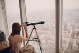 Woman looks telescope through window of skyscraper