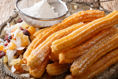 Freshly hot churros with powdered sugar and candied fruits close-up. horizontal