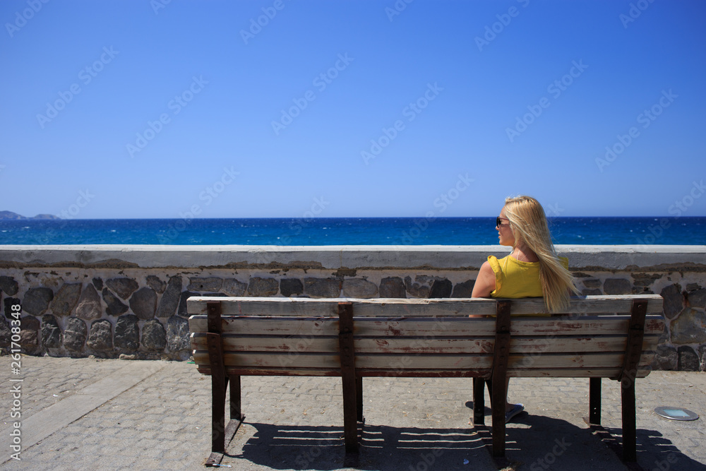 Young woman yellow t-shirt resting on the seafront on a wooden bench