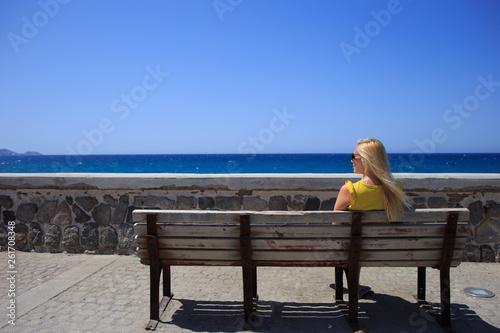 Young woman yellow t-shirt resting on the seafront on a wooden bench © Alfira