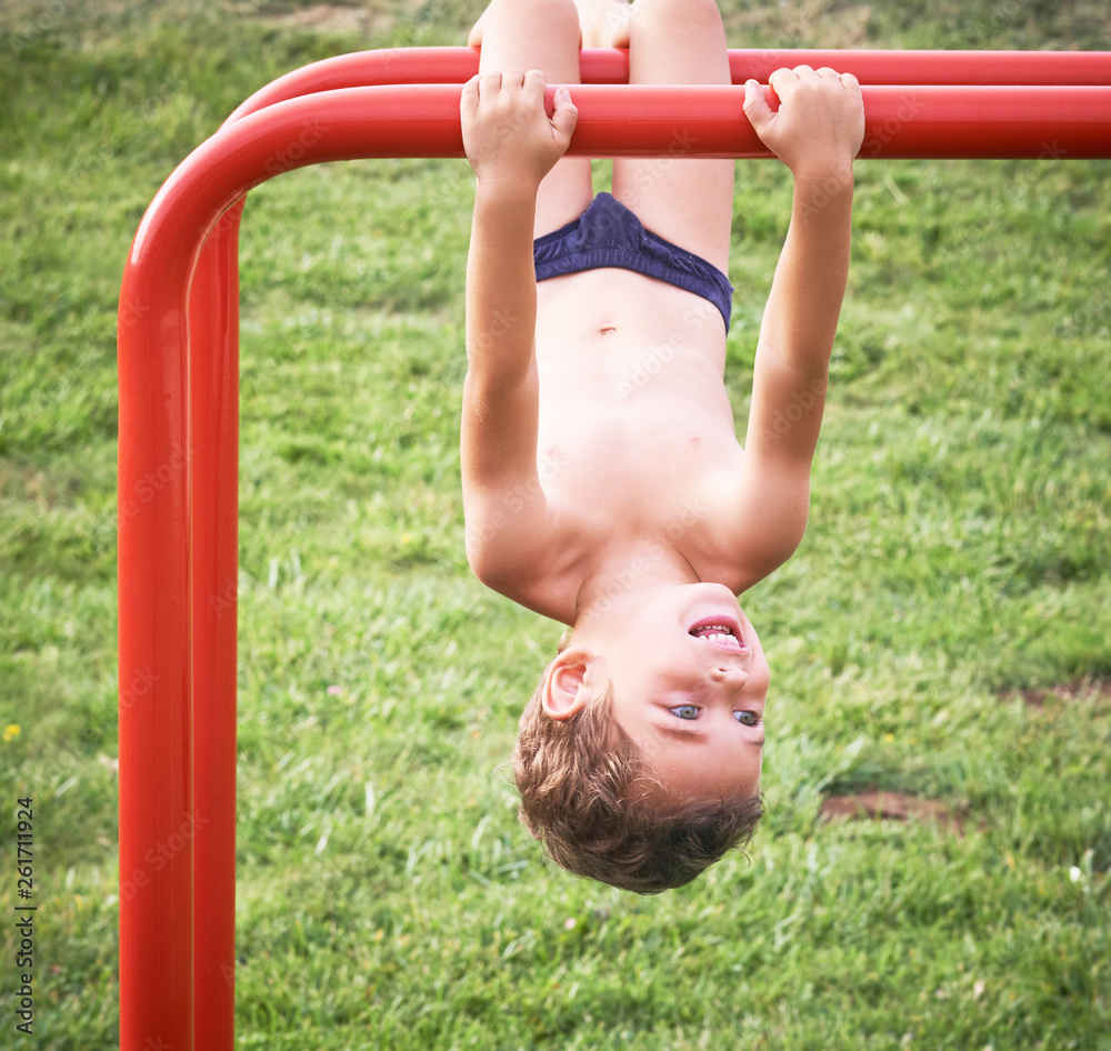 Obraz premium Child on monkey bars. Kid at beach playground. Little boy hanging on gym activity center of preschool play ground. Healthy outdoor activity for kids. Sport for young children.