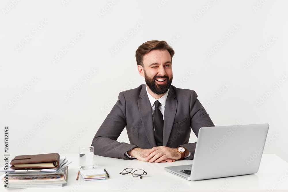 Positive optimistic successful bearded businessman, top manager smiling winks with approval sitting with hands folded on the desktop in office, dressed in a expensive suit with a tie, has a good watch Positive optimistic successful bearded businessman, top manager smiling winks with approval sitting with hands folded on the desktop in office, dressed in a expensive suit with a tie, has a good watch