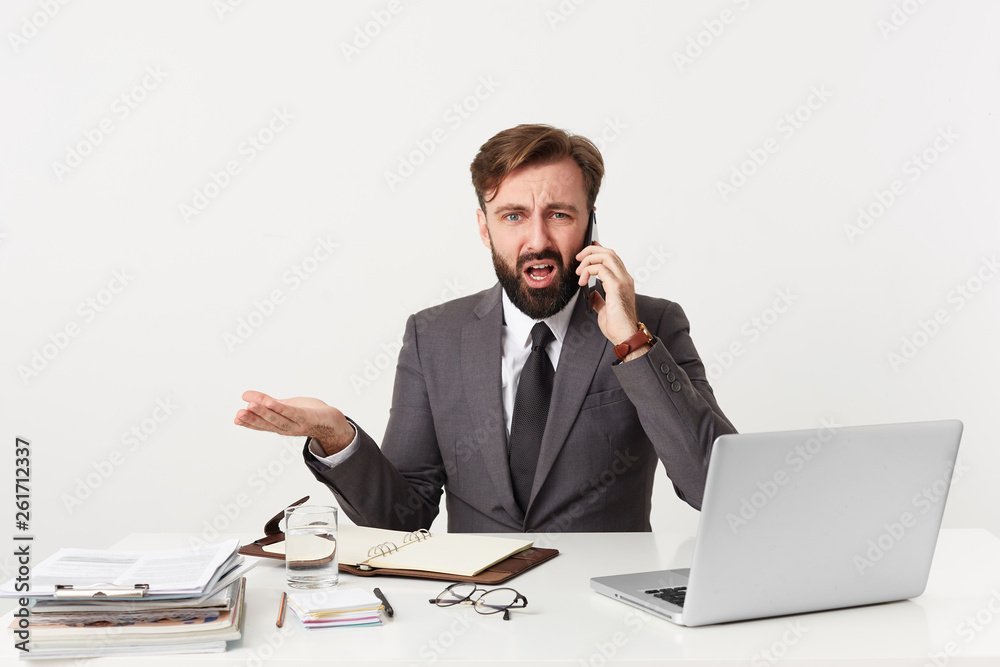 Respectable worthy company manager sitting at desktop, has unpleasant telephone conversation, feels angry, he is told absurd ridiculous nonsensical things, dressed in a suit with a tie, has beard Respectable worthy company manager sitting at desktop, has unpleasant telephone conversation, feels angry, he is told absurd ridiculous nonsensical things, dressed in a suit with a tie, has beard