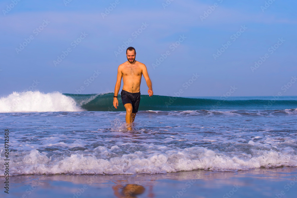 young attractive and happy man with beard and swimming trunks at tropical paradise desert beach alone playful and cheerful in sea water enjoying Summer holidays