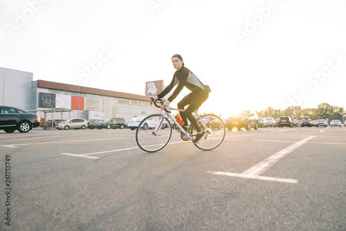 Young rider rides a bicycle in the city on the background of the sunset and looks at the camera. Portrait of a cyclist in motion on road bike riding.