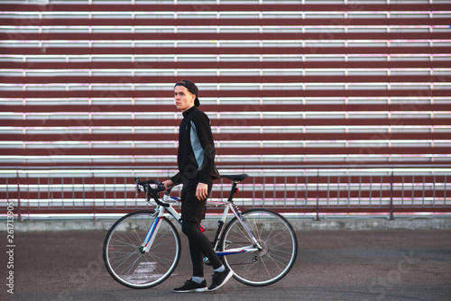 Fototapeta Naklejka Na Ścianę i Meble -  Portrait of an attractive young cyclist in red clothes against a background of striped, modern, bright background. Guy with a bike on a cyberpunk background. Copyspace