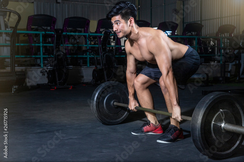 Young man looking focused while lifting heavy weights during a workout session in a dark gym - Image