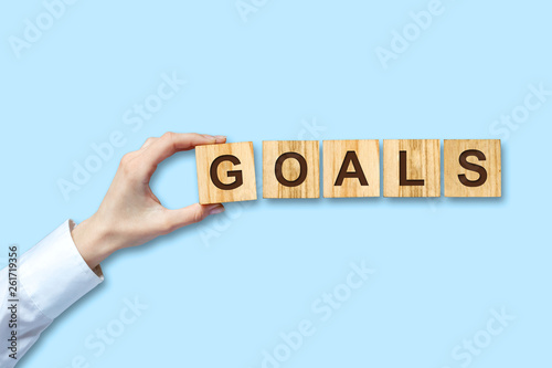 Concept, Goal. Female hand in a white shirt holds in her hand a wooden block with the inscription, Goal. Blue background. Isolated. Business background.
