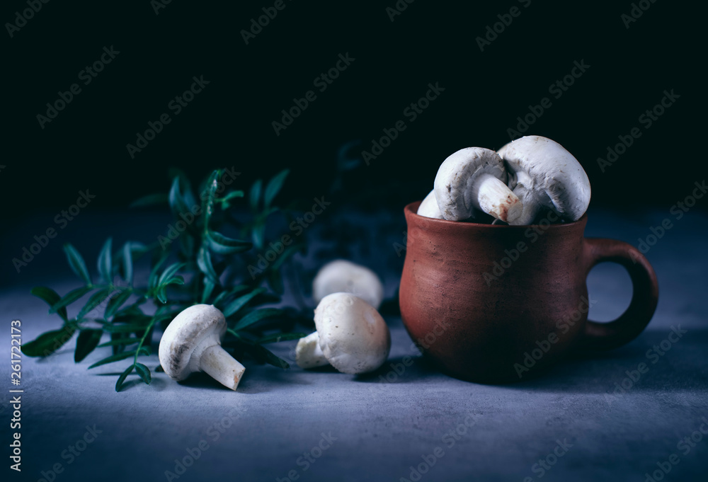 Obraz premium champignon mushrooms in an old clay pot on a table in a dark