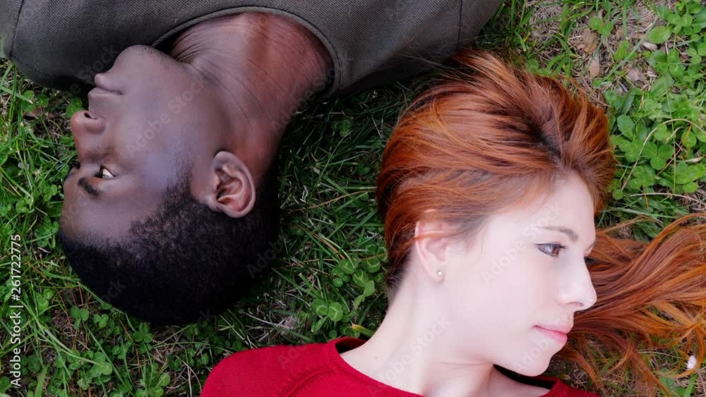 Mixed young couple lying on lawn turning heads in opposite site. Crisis,problems