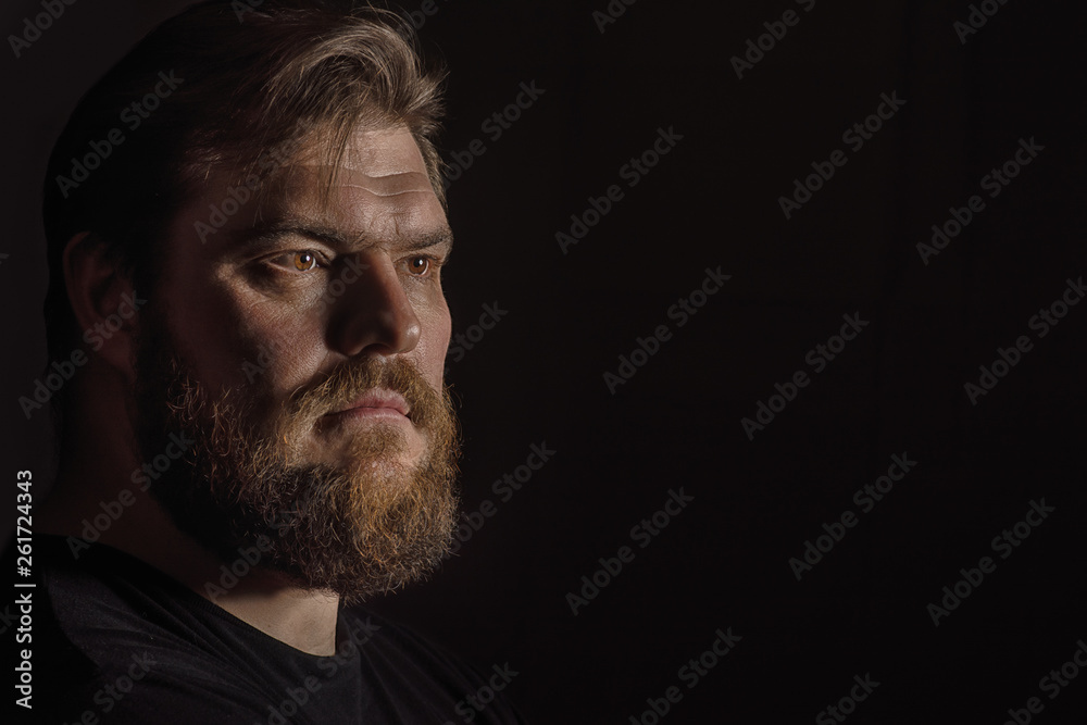 Close-up face profile portrait strong serious brutal bearded man on black. Confident and dramatic concept