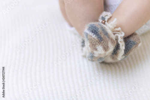 Newborn baby feet close up in wool brown knitted socks booties on a white blanket. The baby is in the crib