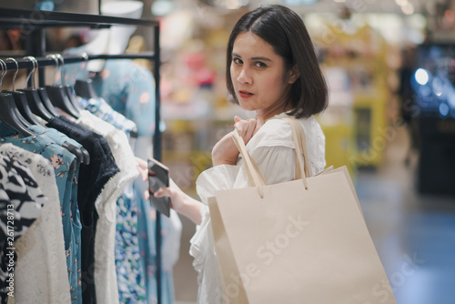 Young Asian beautiful woman shot hair smiling shopping new clothes in a shopping mall store. Woman standing and holding a shopping bag and in the store and looking at camera.