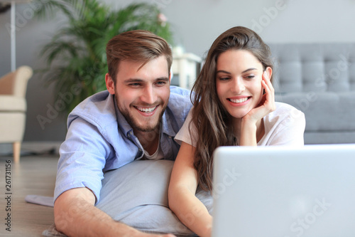 Young couple doing some online shopping at home, using a laptop on floor.