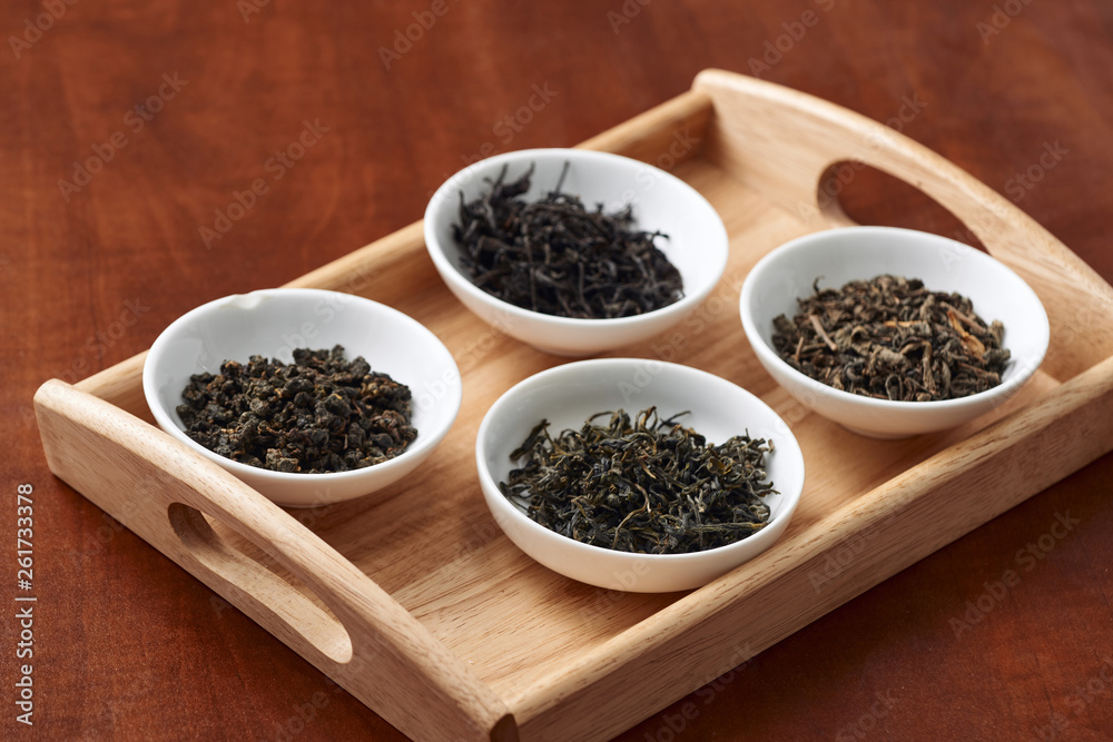 the white drinking bowls of assortment of dry tea in order on wooden background the white drinking bowls of assortment of dry tea in order on wooden background