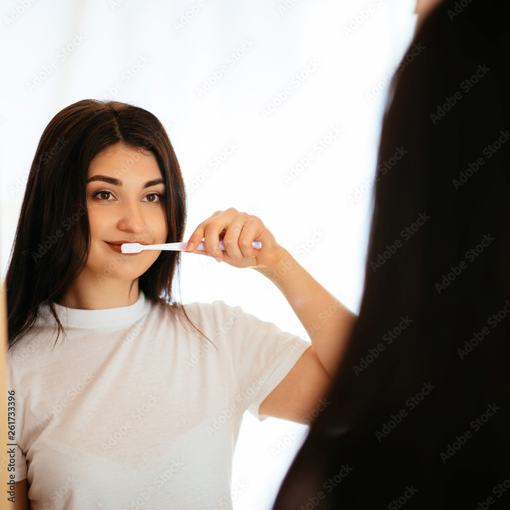 Beautiful young woman with toothbrush cleaning teeth at bathroom. Dental treatment. Dentistry, beauty and body care Beautiful young woman with toothbrush cleaning teeth at bathroom. Dental treatment. Dentistry, beauty and body care