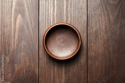 Empty wooden bowl on brown background. Round salad-bowl on wooden table. Top view