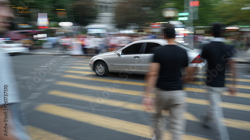 Pedestrians in motion blur crossing a city street while the car is driving at a red light