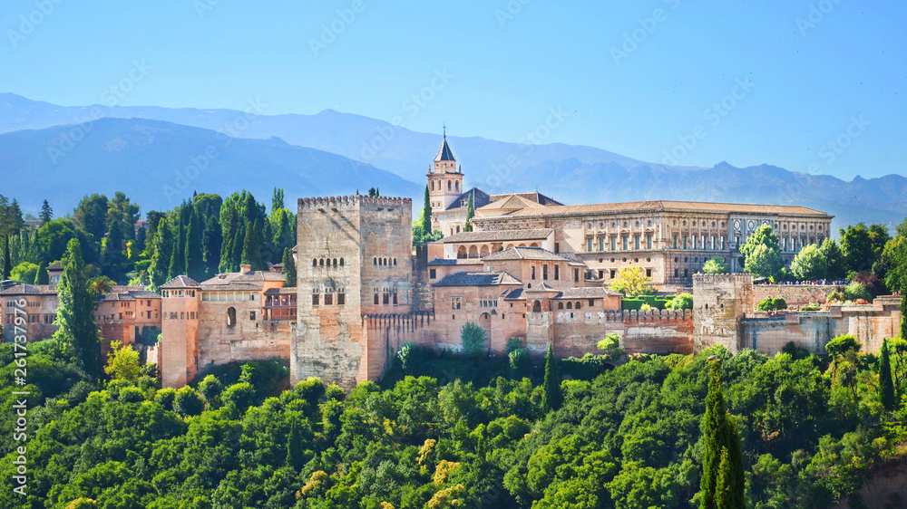Beautiful Alhambra Palace complex in Spanish Granada on a sunny day captured on 16:9 photography. The amazing fortress and popular tourist spot is surrounded by green woods and mountains.