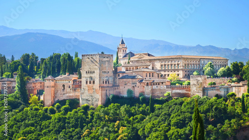 Beautiful Alhambra Palace complex in Spanish Granada on a sunny day captured on 16:9 photography. The amazing fortress and popular tourist spot is surrounded by green woods and mountains.