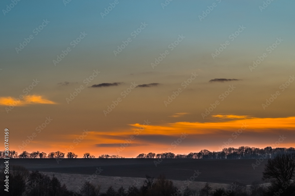 Sunset over the early spring fields and bare trees
