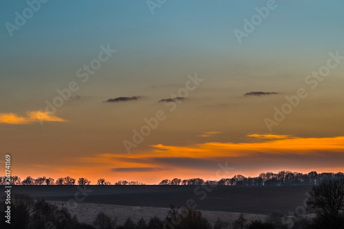 Sunset over the early spring fields and bare trees