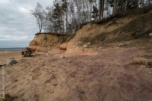 Fototapeta Naklejka Na Ścianę i Meble -  Limestone beach at the Baltic Sea with beautiful sand pattern and vivid red and orange color - Tourist writings on the walls and rocks and sand - Veczemju Klintis, Latvia - April 13, 2019