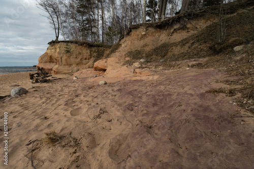 Limestone beach at the Baltic Sea with beautiful sand pattern and vivid red and orange color - Tourist writings on the walls and rocks and sand - Veczemju Klintis, Latvia - April 13, 2019