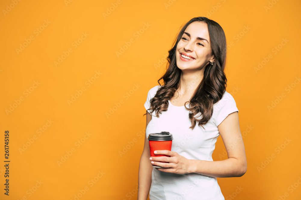 Invigorating coffee. Fabulous girl with the red cup in her hand full of coffee is smiling right next to the spicy-colored background. Invigorating coffee. Fabulous girl with the red cup in her hand full of coffee is smiling right next to the spicy-colored background.