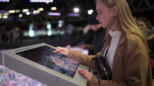 Woman using interactive touchscreen display at urban exhibition - scrolling and touching. Entertainment and technology concept