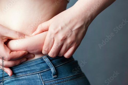 woman's hand holding excessive belly fat, the concept of weight loss